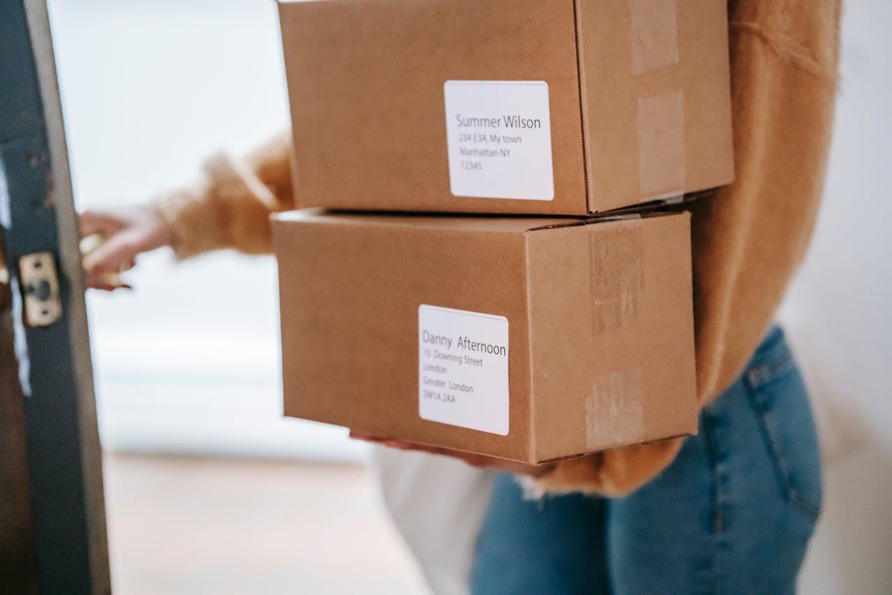 A woman delivering two cardboard boxes to an apartment indoors.