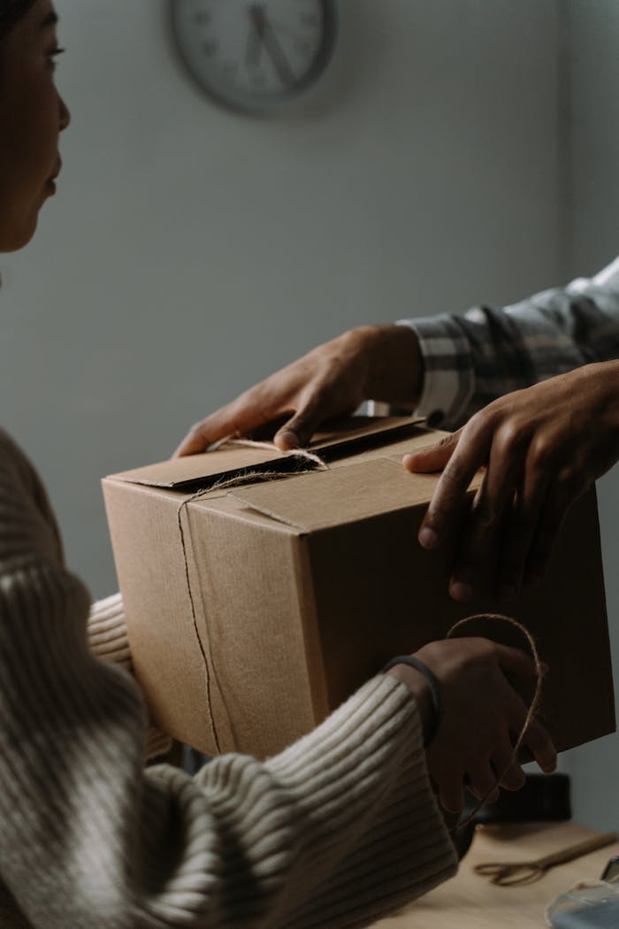 A close-up image featuring hands exchanging a cardboard box in an indoor setting.